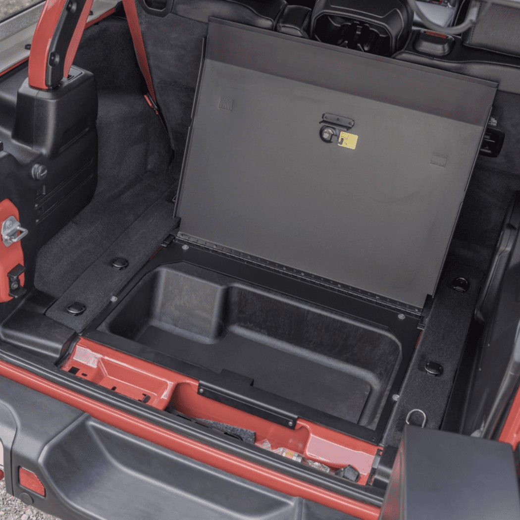 Open Tuffy Locking Cubby Cover installed in the rear cargo floor of a Jeep Wrangler JL, revealing the hidden storage compartment beneath.