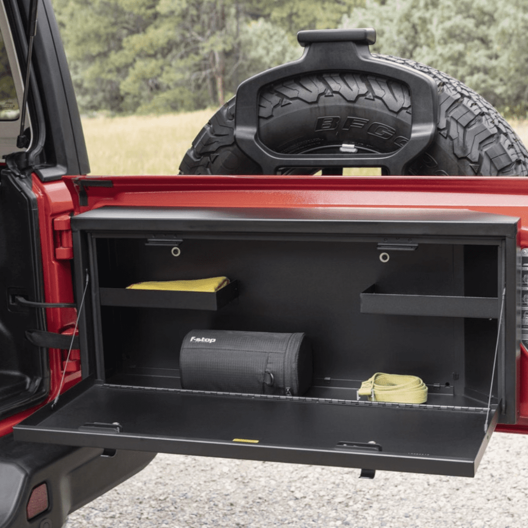Tailgate Lockbox open with gear stored inside, including recovery straps and tools, illustrating how the fold-down door doubles as a work surface.